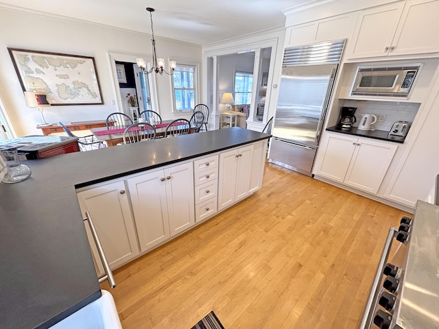 kitchen featuring built in appliances, dark countertops, a chandelier, light wood-type flooring, and white cabinets