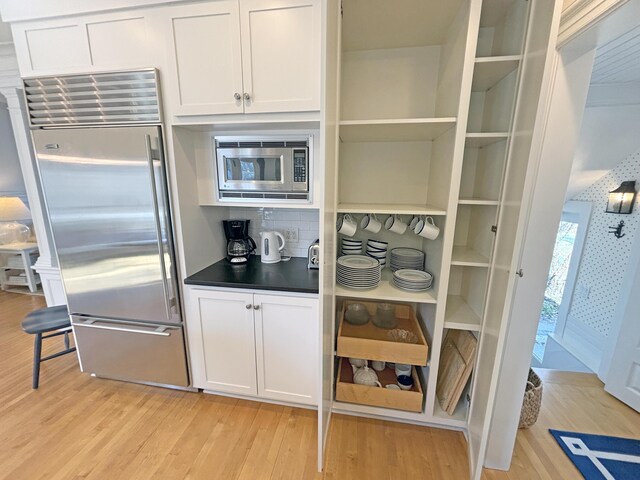 kitchen with built in appliances, light wood-style flooring, decorative backsplash, dark countertops, and white cabinetry