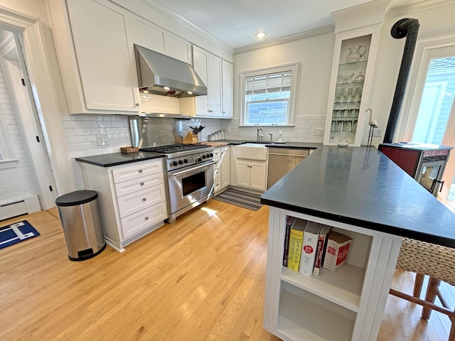 kitchen with appliances with stainless steel finishes, wall chimney exhaust hood, a sink, dark countertops, and ornamental molding