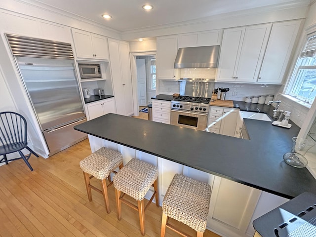 kitchen featuring extractor fan, built in appliances, a sink, white cabinetry, and crown molding