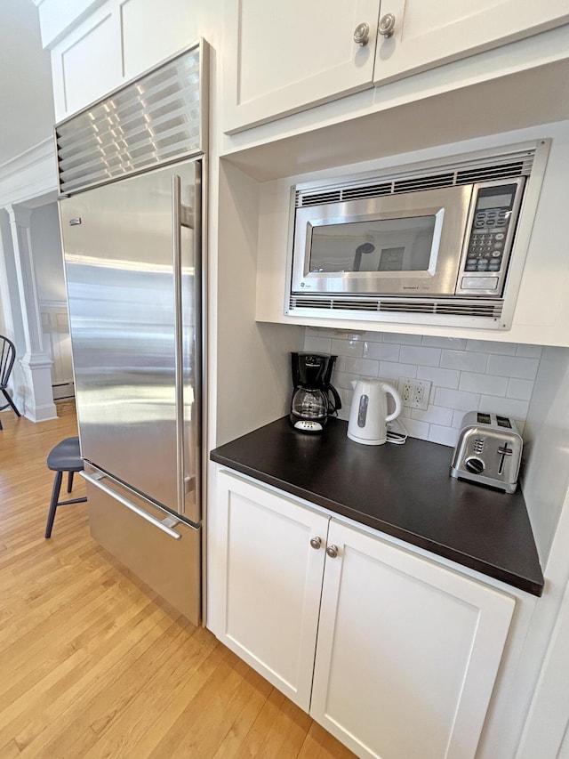 kitchen featuring built in appliances, light wood-style floors, white cabinets, dark countertops, and decorative backsplash