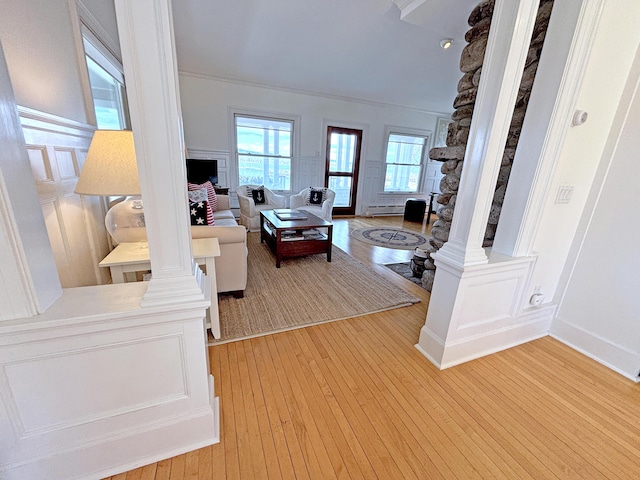 living room featuring light wood-style flooring, ornate columns, crown molding, and baseboard heating