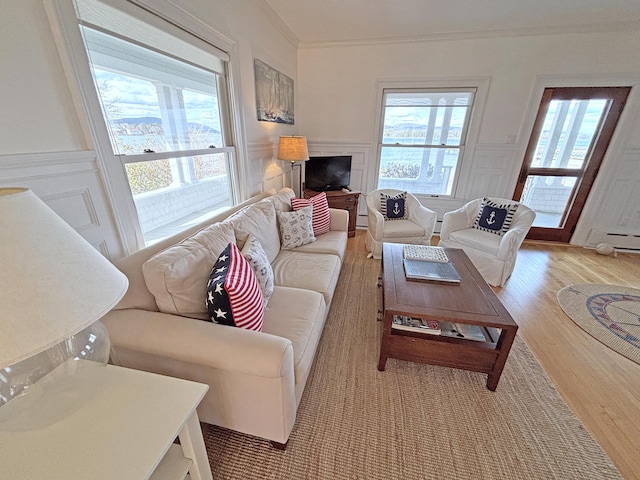 living room with light wood-style floors, plenty of natural light, crown molding, baseboard heating, and a decorative wall