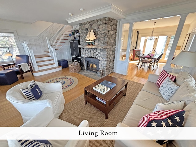 living area featuring ornate columns, a chandelier, wood finished floors, crown molding, and stairs