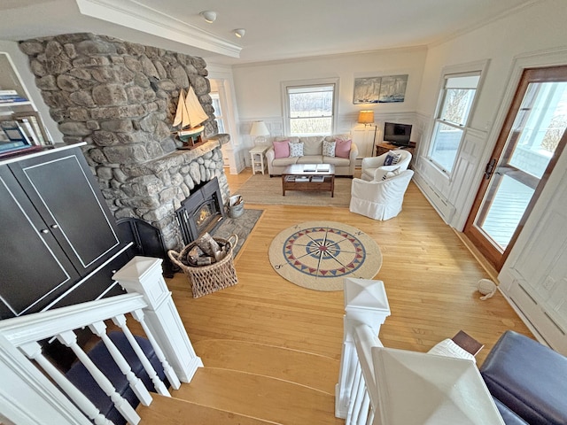 living room featuring a stone fireplace, ornamental molding, light wood-type flooring, plenty of natural light, and wainscoting