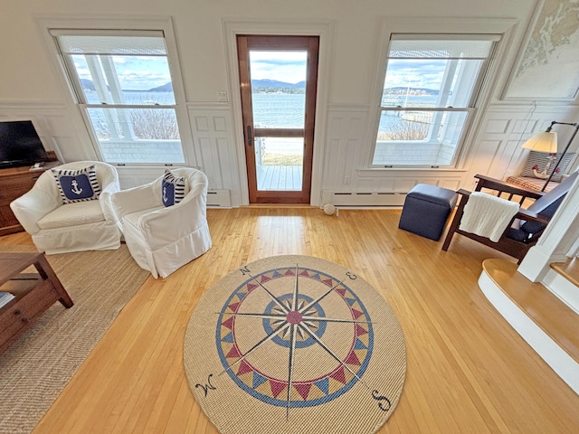 living room with a decorative wall, light wood-type flooring, baseboard heating, a wainscoted wall, and a baseboard heating unit