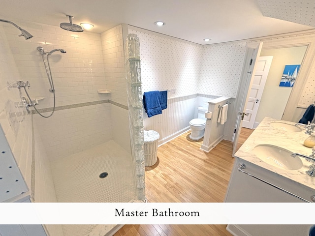 bathroom with wood finished floors, tiled shower, toilet, and double vanity