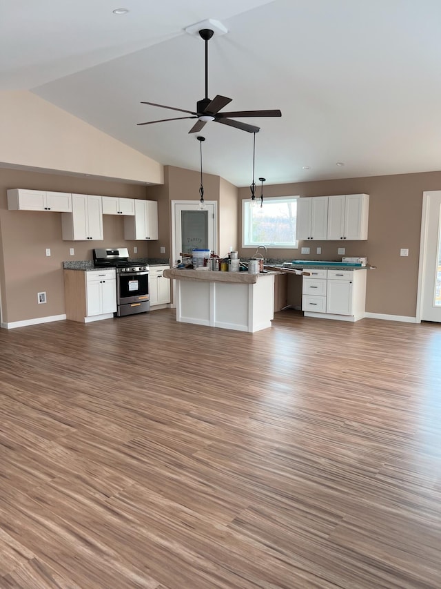 kitchen featuring stainless steel gas stove, vaulted ceiling, ceiling fan, baseboards, and wood finished floors