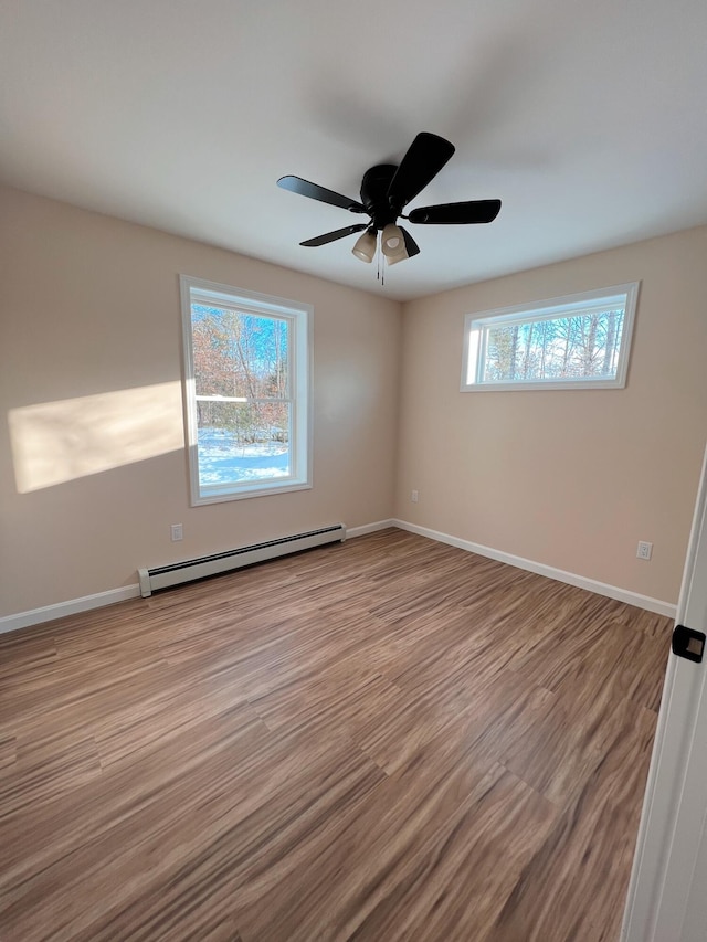empty room with a baseboard heating unit, baseboards, wood finished floors, and a ceiling fan