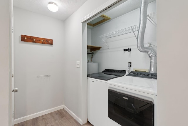 laundry room featuring washer and clothes dryer, light wood-style flooring, baseboards, and a textured ceiling