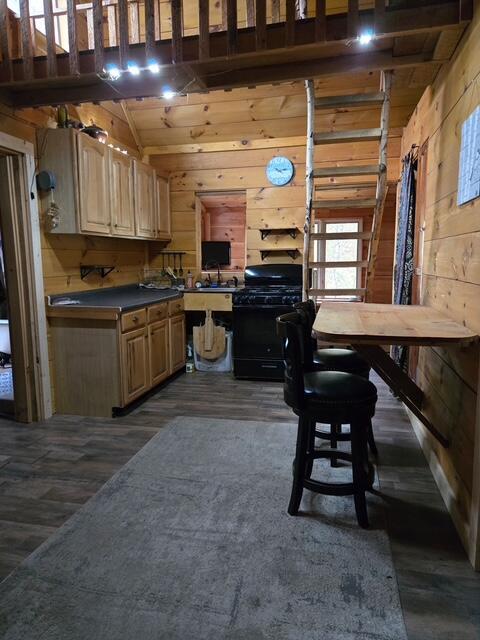 103 Fellows Ln, Winthrop, ME 04364 - kitchen featuring black range with gas stovetop, wooden walls, dark wood-type flooring, dark countertops, and lofted ceiling