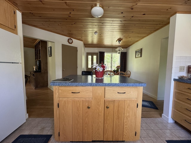 898 Sebec Village Rd, Sebec, ME 04481 - kitchen with freestanding refrigerator, wood ceiling, dark countertops, light tile patterned floors, and a kitchen island