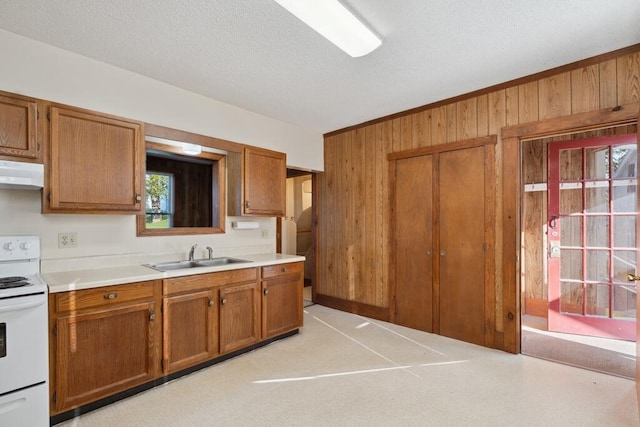 kitchen featuring white range with electric stovetop, a sink, wood walls, under cabinet range hood, and brown cabinets