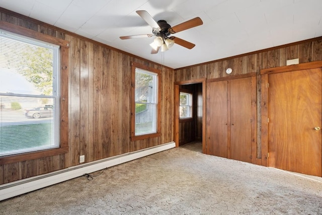 carpeted spare room featuring a baseboard heating unit, a ceiling fan, wooden walls, and ornamental molding