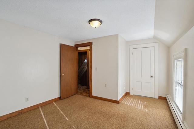 unfurnished bedroom featuring a baseboard heating unit, multiple windows, carpet floors, baseboards, and vaulted ceiling