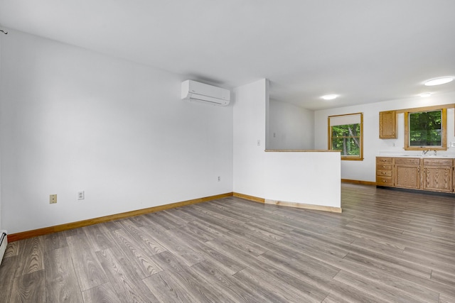 32 Thorne Ave, Lewiston, ME 04240 - unfurnished living room featuring a wall mounted AC, baseboards, wood finished floors, and a sink