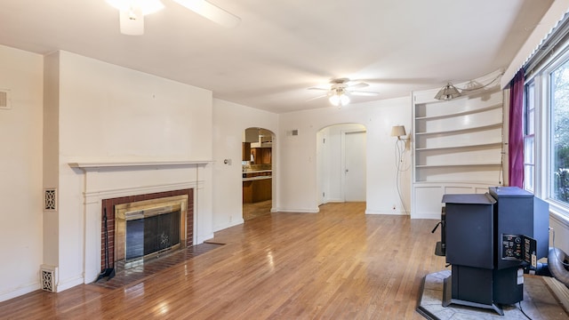 13 Packard Ave, Norway, ME 04268 - unfurnished living room with ceiling fan, arched walkways, light wood-style floors, a tiled fireplace, and baseboards