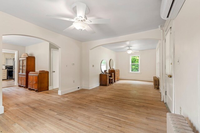 24 Emery Corner Rd, Limerick, ME 04048 - unfurnished living room featuring radiator heating unit, a wall mounted air conditioner, ceiling fan, arched walkways, and light wood finished floors
