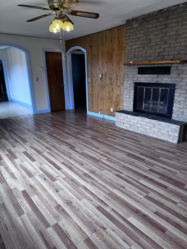 1596 Bald Mountain Rd, Orland, ME 04472 - unfurnished living room with arched walkways, baseboards, ceiling fan, wood finished floors, and a brick fireplace