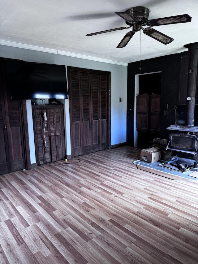 1596 Bald Mountain Rd, Orland, ME 04472 - unfurnished living room featuring a wood stove, wood finished floors, a ceiling fan, baseboards, and crown molding