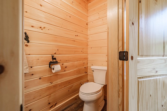 bathroom with toilet, wood walls, and wood finished floors
