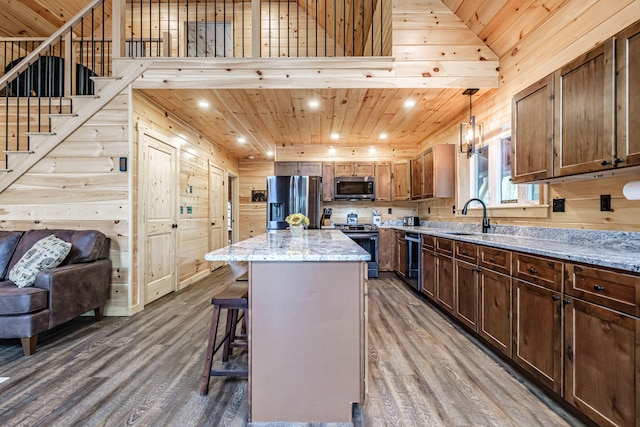 kitchen with appliances with stainless steel finishes, wood finished floors, a sink, a kitchen breakfast bar, and wooden ceiling