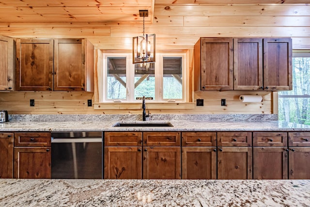 kitchen with stainless steel dishwasher, a sink, plenty of natural light, hanging light fixtures, and wooden walls