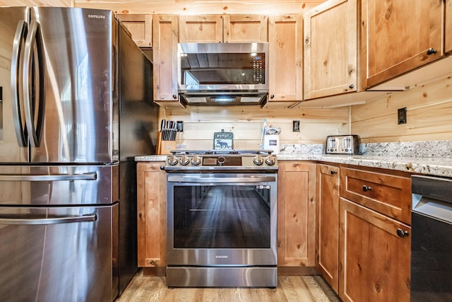 kitchen with stainless steel appliances, light wood-type flooring, and light stone counters