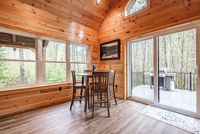 dining area with plenty of natural light, wood finished floors, wooden walls, and lofted ceiling