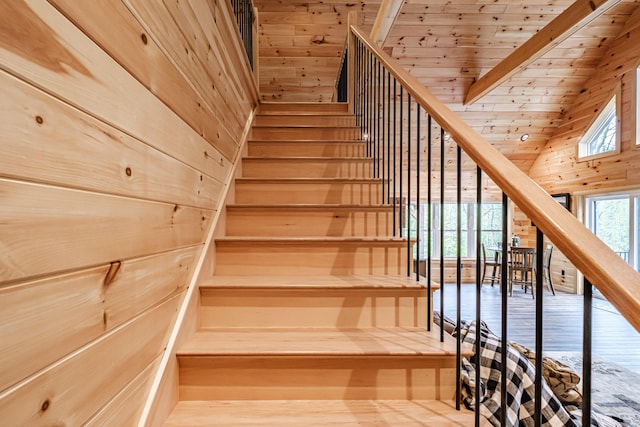 staircase with wooden walls, high vaulted ceiling, and wooden ceiling