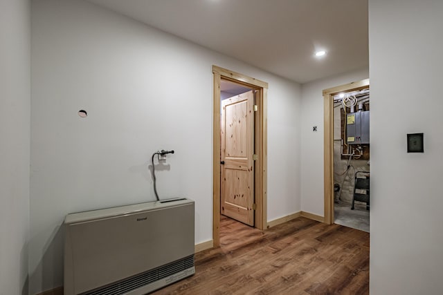 corridor featuring wood finished floors, heating unit, recessed lighting, baseboards, and tankless water heater