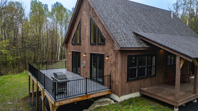 back of house featuring roof with shingles, a wooden deck, and a lawn