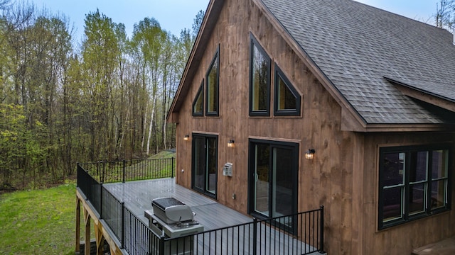 back of property featuring roof with shingles, a wooden deck, and a yard