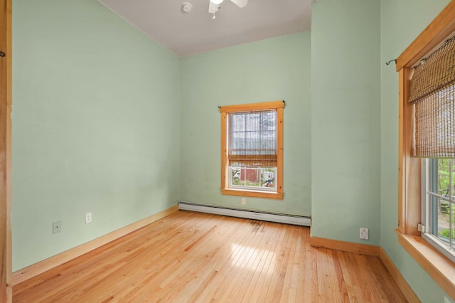 spare room featuring baseboard heating, hardwood / wood-style floors, baseboards, and a ceiling fan