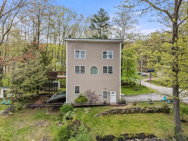 back of property featuring a wooden deck, a chimney, and a lawn