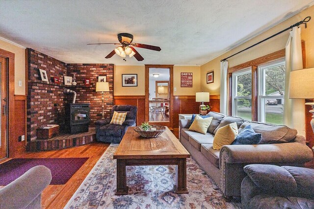 286 Canaan Rd, Clinton, ME 04927 - living room featuring wood finished floors, a ceiling fan, a wood stove, wainscoting, and a textured ceiling
