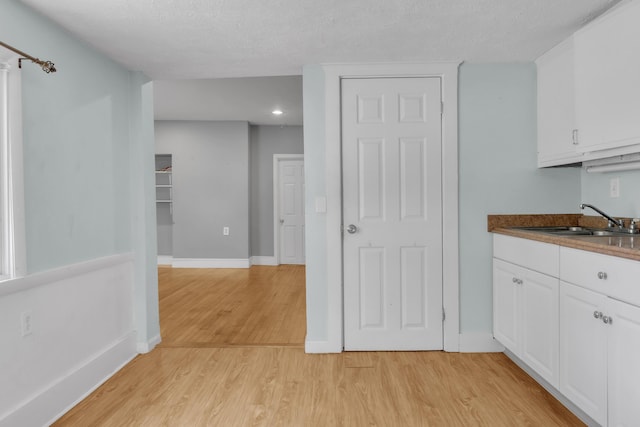 138 Summer St, Biddeford, ME 04005 - kitchen featuring light wood-style floors, white cabinetry, a sink, a textured ceiling, and baseboards