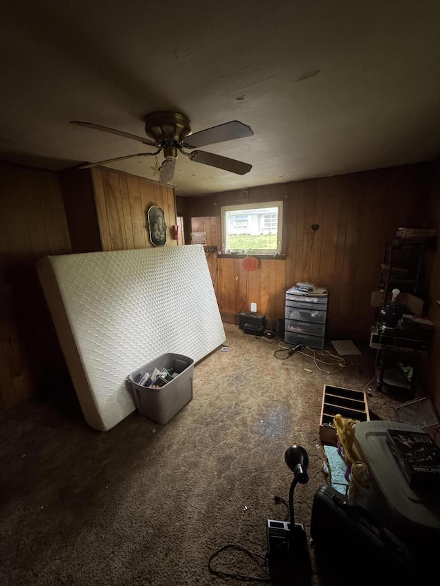 carpeted bedroom featuring wood walls and a ceiling fan