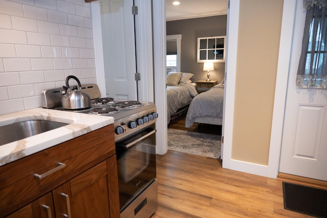 750 Roosevelt Trl Unit 7, Naples, ME 04055 - kitchen with stainless steel gas stove, brown cabinetry, decorative backsplash, light wood finished floors, and light stone counters