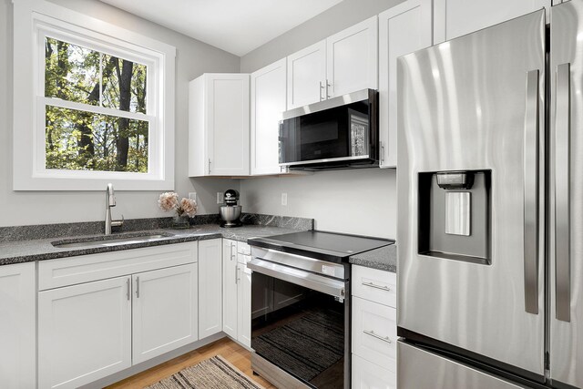 14 Depot St, Buxton, ME 04093 - kitchen with stainless steel appliances, a sink, white cabinetry, light wood-type flooring, and dark stone counters