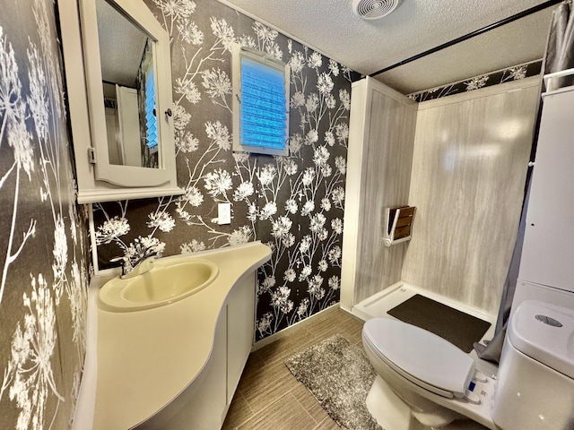 bathroom with wallpapered walls, toilet, a textured ceiling, vanity, and baseboards
