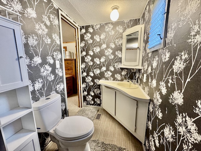 bathroom with a textured ceiling, toilet, vanity, and wallpapered walls