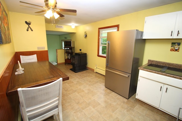 kitchen featuring freestanding refrigerator, a baseboard radiator, a ceiling fan, white cabinets, and a wood stove