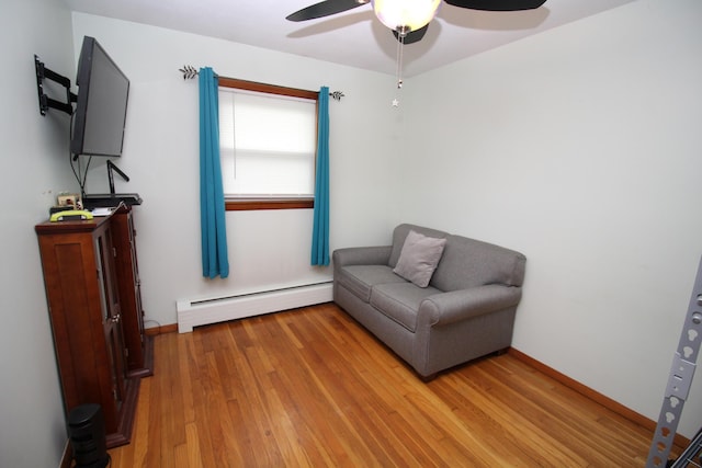 sitting room with a baseboard heating unit, a ceiling fan, light wood finished floors, and baseboards