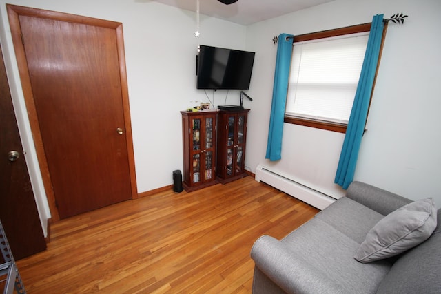 living area featuring baseboard heating, light wood-style floors, ceiling fan, and baseboards