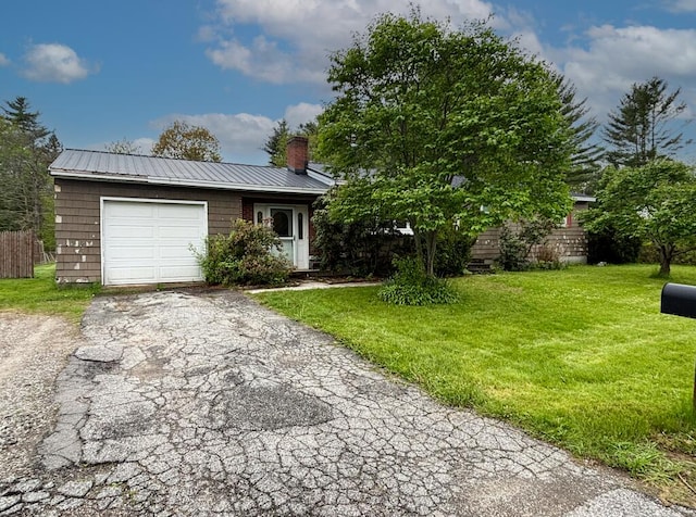 view of front of home featuring a chimney, an attached garage, driveway, a front yard, and metal roof