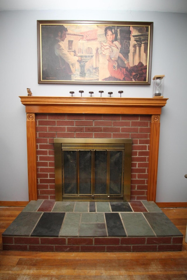detailed view of a fireplace, baseboards, and wood finished floors