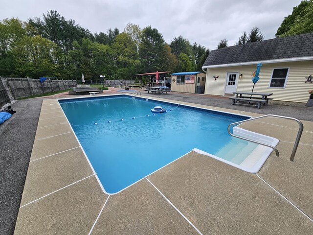 view of pool featuring a patio area, an outbuilding, an exterior structure, and a diving board