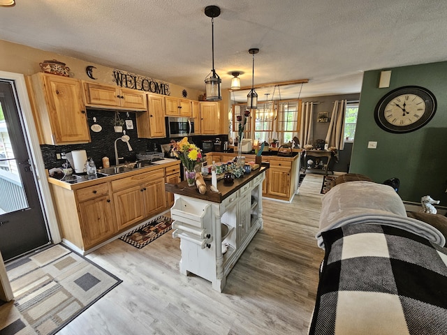 kitchen with stainless steel microwave, a sink, light wood-type flooring, a textured ceiling, and tasteful backsplash
