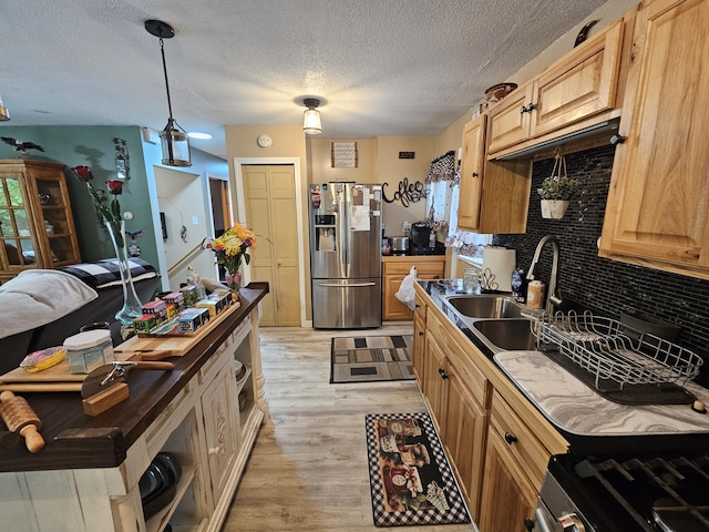 kitchen with stainless steel appliances, a sink, decorative backsplash, a textured ceiling, and light wood-type flooring